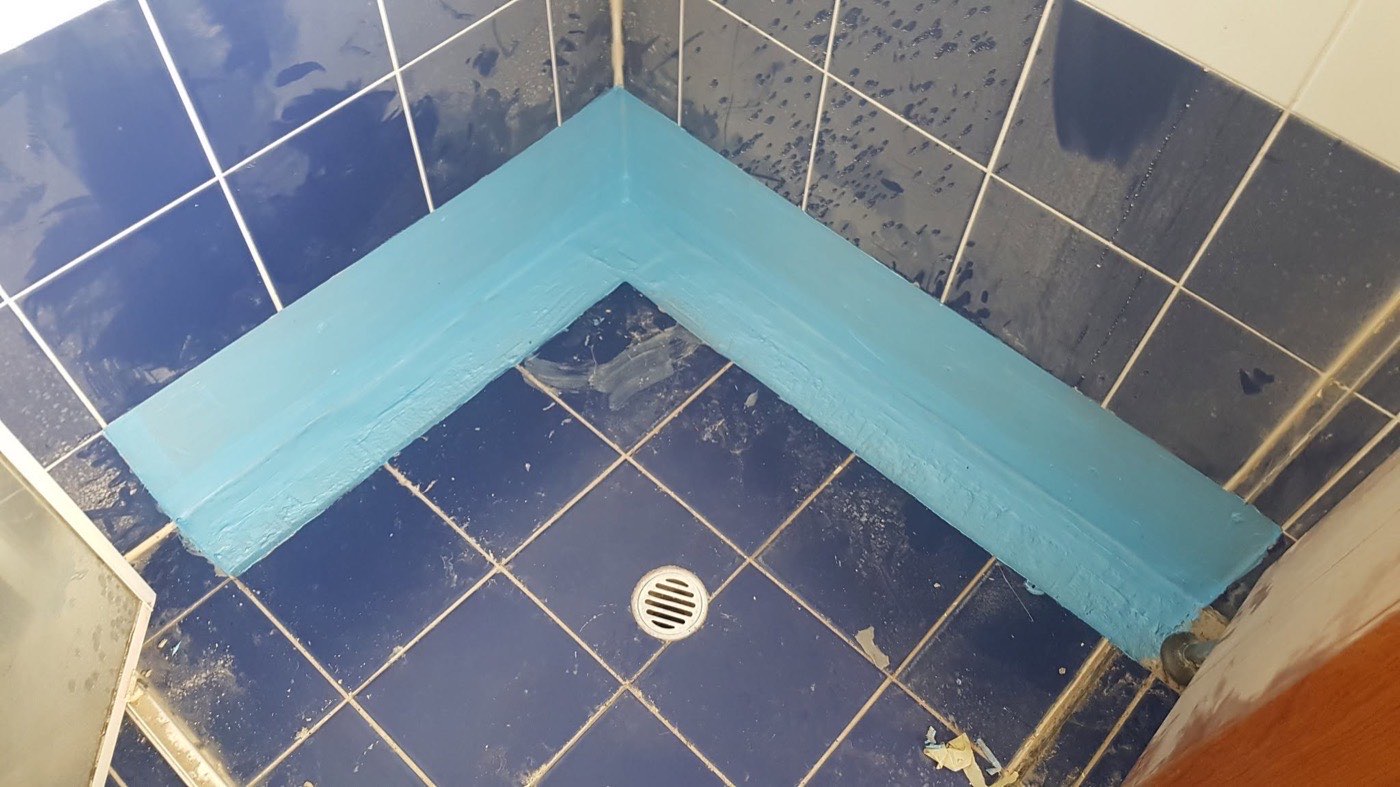 A tiled shower recess with blue waterproofing applied along the floor join