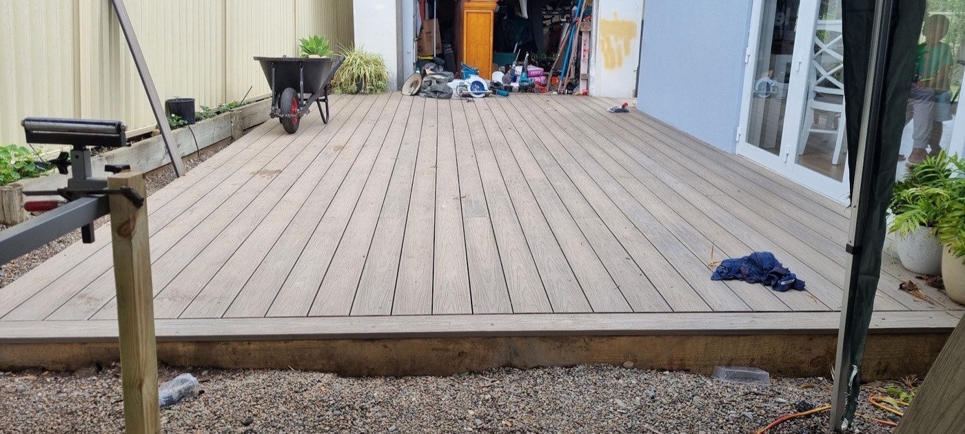 A finished timber deck running along the back of a house, with tools still on it