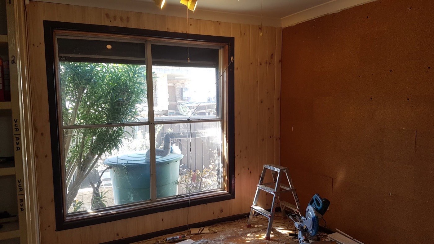 A room with fresh timber wall lining around a black-framed window