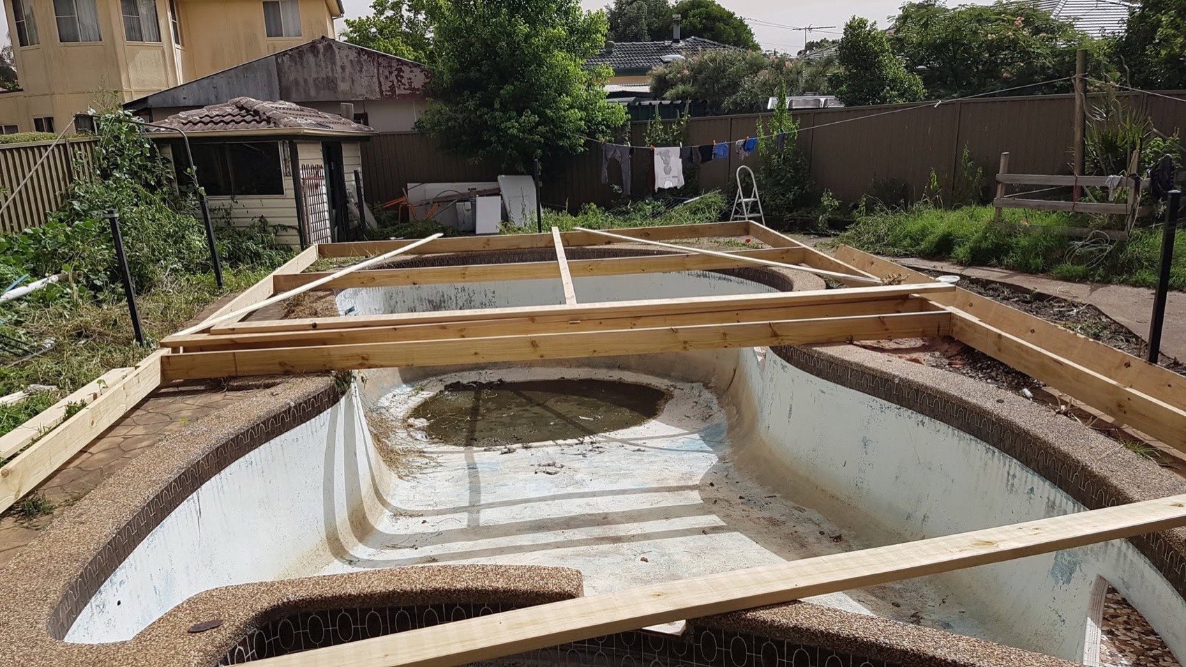 A timber deck frame being built out over an old backyard pool