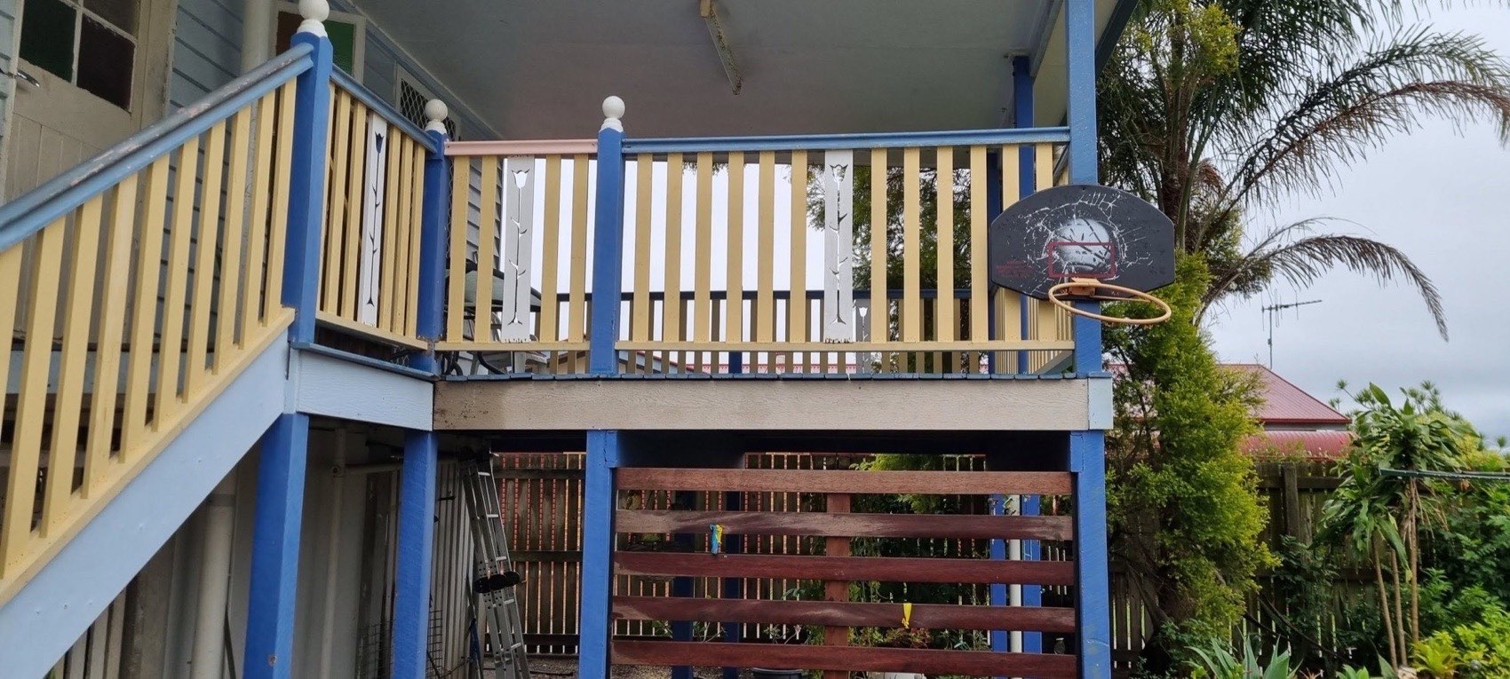 A raised home with a rebuilt timber balustrade beside a palm tree