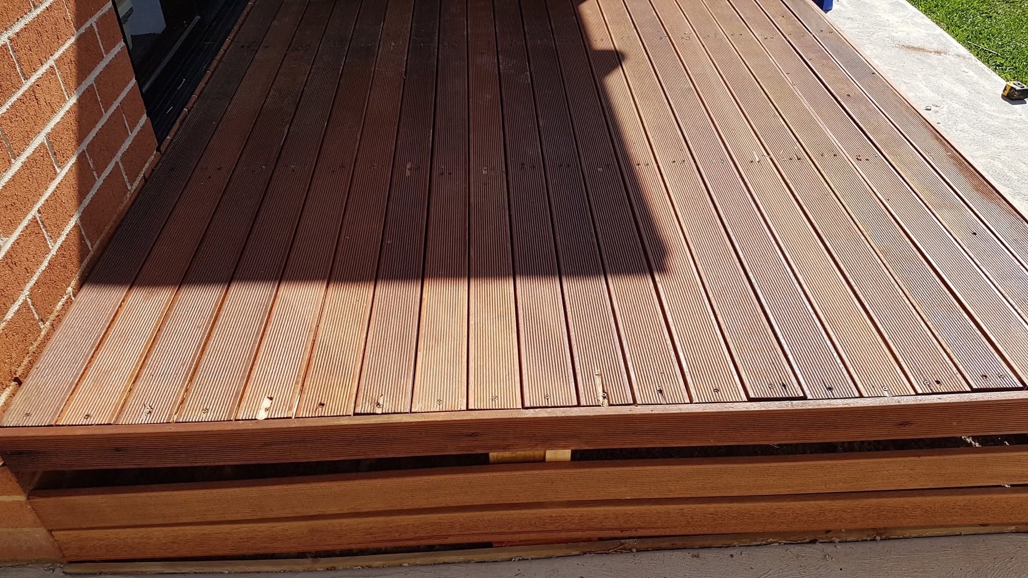 A finished hardwood deck stained a deep red-brown, lit by afternoon sun