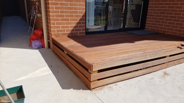 A finished timber deck against a brick wall and sliding doors