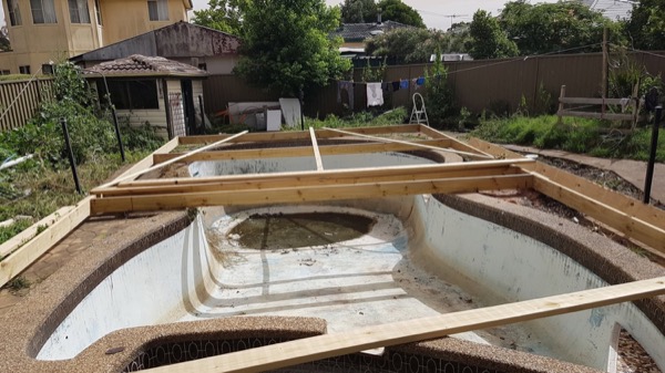 A timber deck frame built out over an old backyard pool