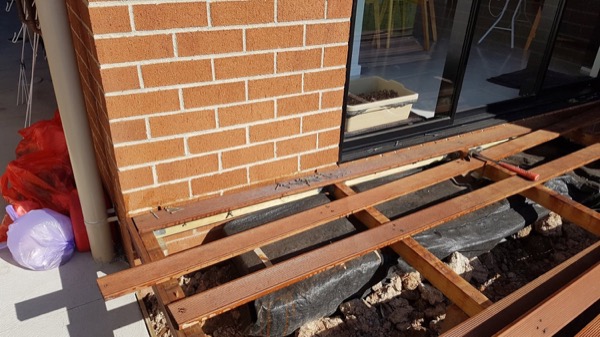 A deck frame fixed against a brick wall beside sliding doors