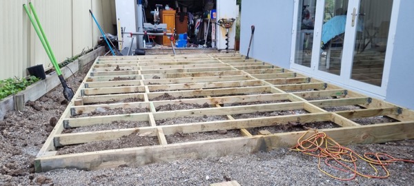 A deck frame laid out on gravel beside a house